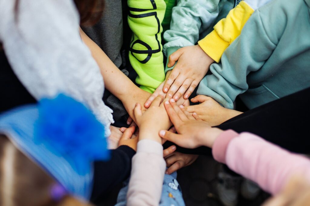 Team of children put hands together and unite to win game in playground. Summer holidays in camp